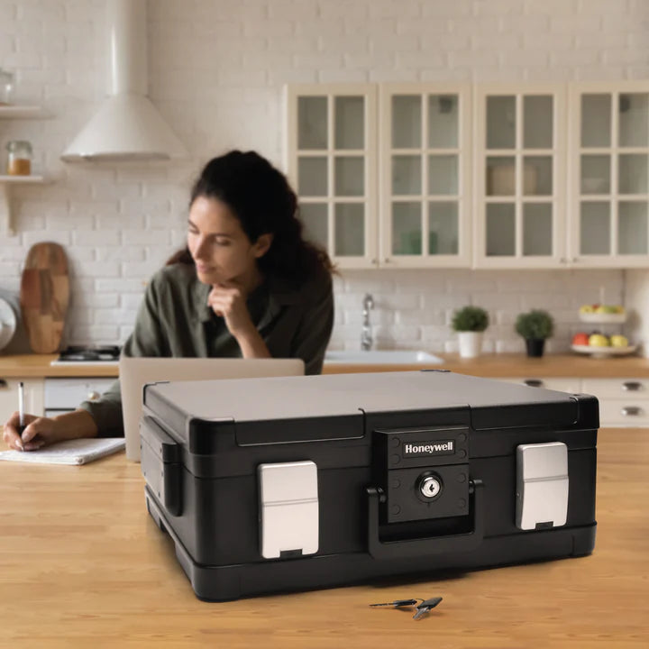 Woman sitting at a kitchen table with a large black Honeywell 1114 Fire & Water Chest in front of her.